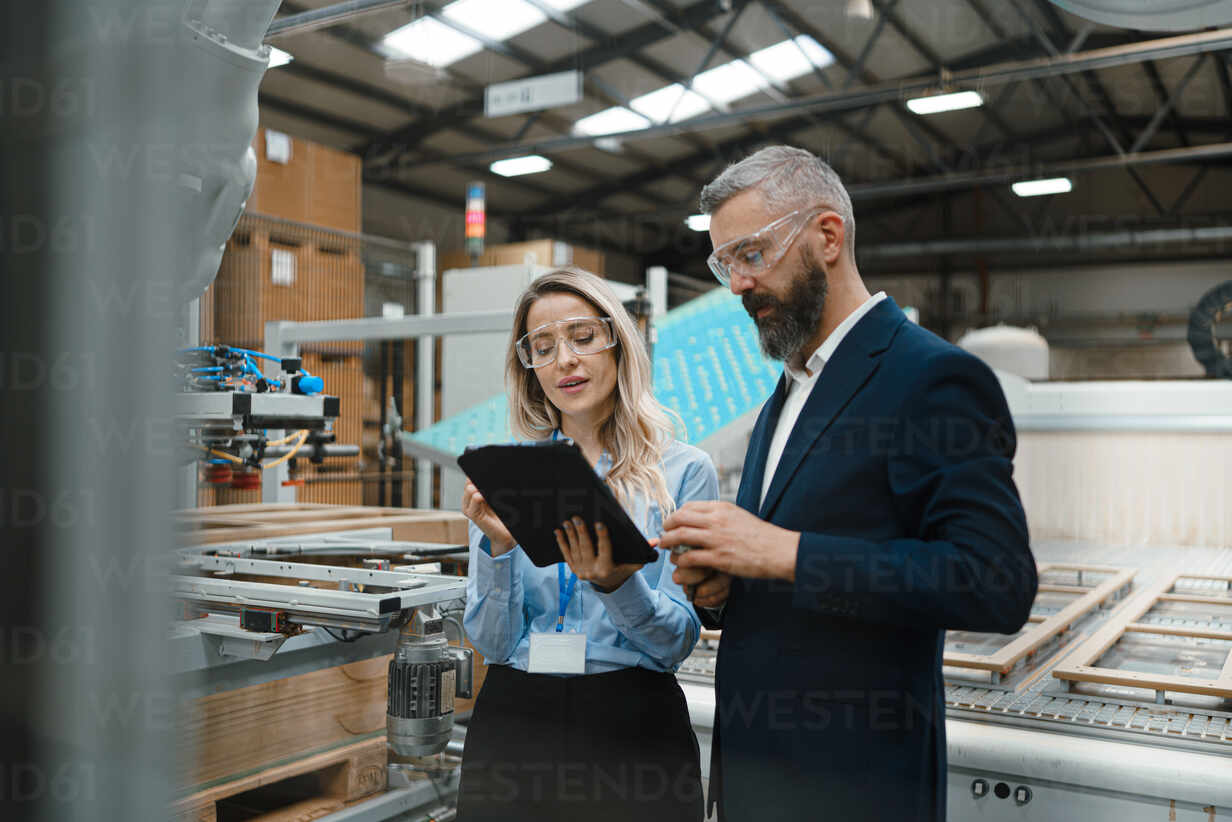 Female engineer and male project manager standing in modern industrial factory, talking about production of wooden furniture. Big furniture manufacturing facility with robotics, robotic arms and automation. Residential Engineer